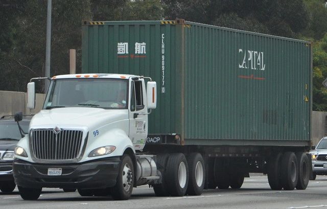 White semi-truck with green container on highway